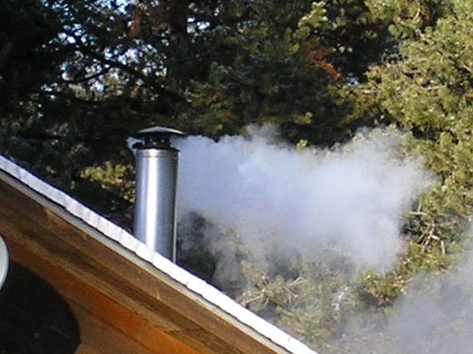 Smoke pours out of a woodstove chimney stack